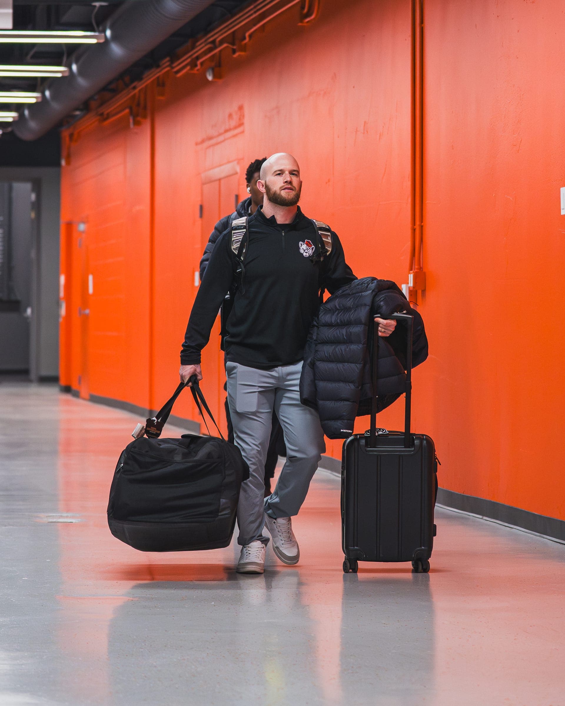 Colin DeClark walking through an arena corridor with team bags on a road trip